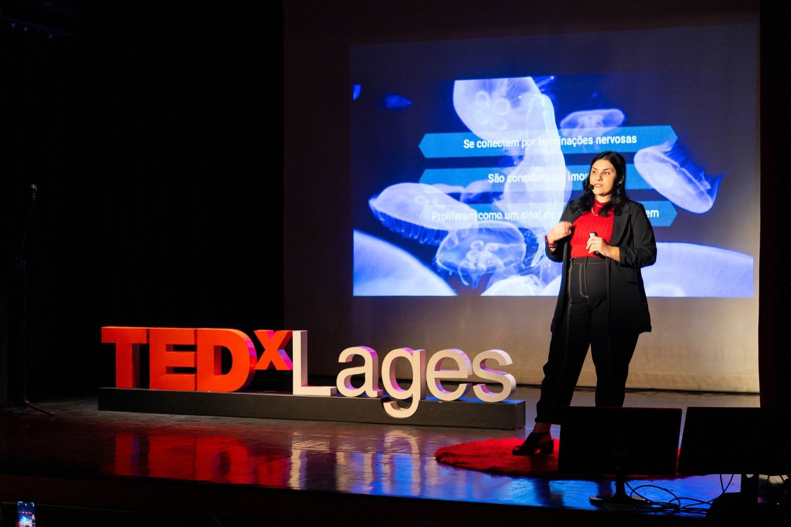 Ludymila Pimenta no palco do TEDx Lages, 2023, com as letras TEDx ao lado